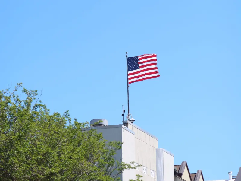 American flag on building with trees and clear sky.