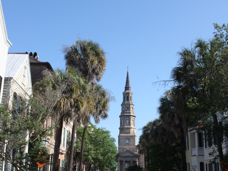 Street view with church steeple, palm trees, and historic buildings under blue sky.